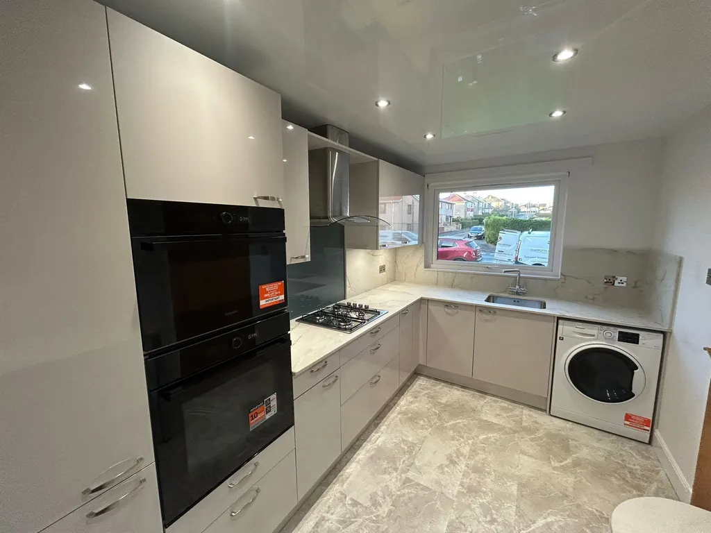 White fitted kitchen with an L-shaped worktop and integrated oven