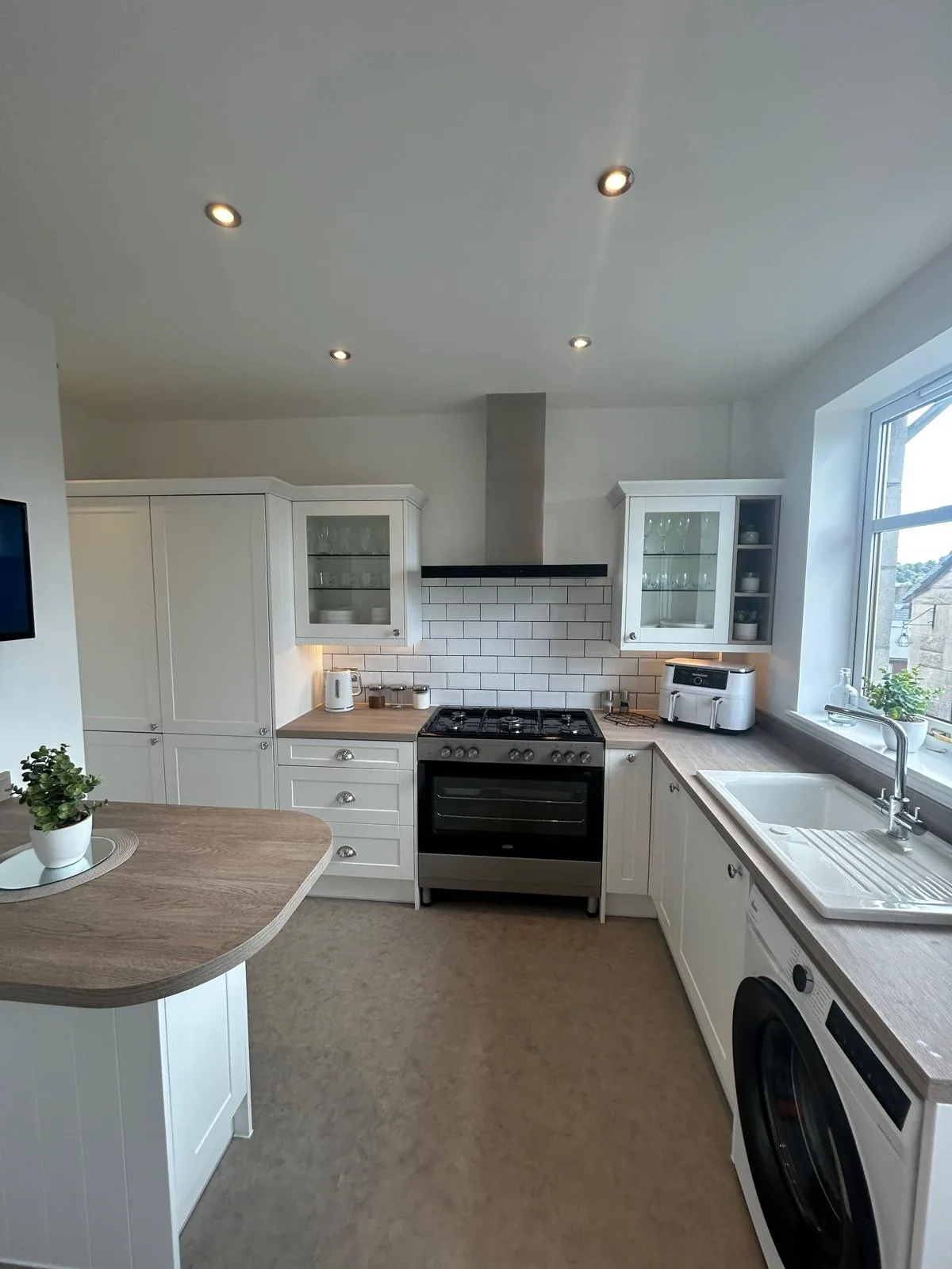 Completed white kitchen with glazed cabinets, wood-effect worktops and a peninsula